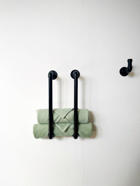 May include: Black metal towel rack with two bars and a single hook mounted on a white wall. Two green towels are folded and hanging on the bars.